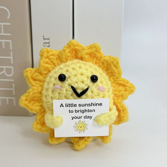 Crocheted sun-shaped plushie holding a card with 'A little sunshine to brighten your day' text.