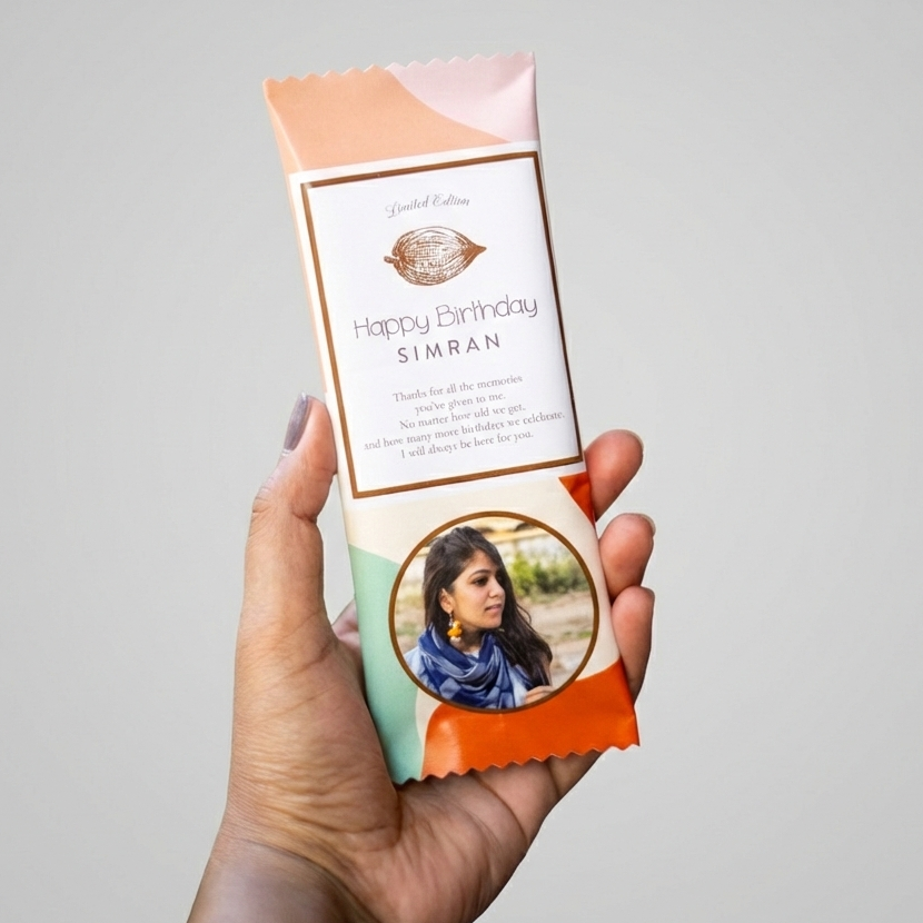 Hand holding a personalized chocolate bar with a photo and 'Happy Birthday Simran' text on a gray background