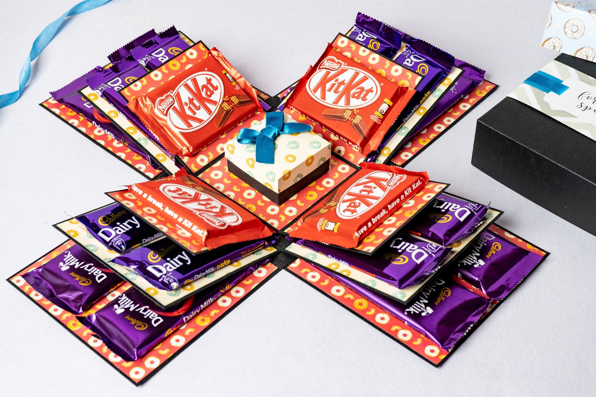 A chocolate explosion box with three layers, featuring a blue donut design on the inside, containing various chocolate packets.