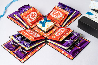 A chocolate explosion box with three layers, featuring a blue donut design on the inside, containing various chocolate packets.