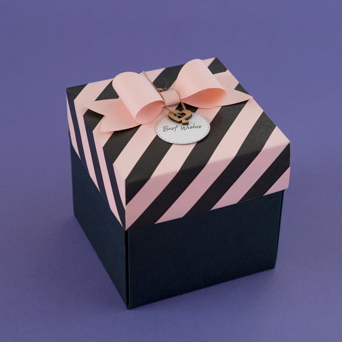 A two-layered baby pink and black striped Explosion Box with a pink ribbon on top, displaying a 'Best Wishes' tag.