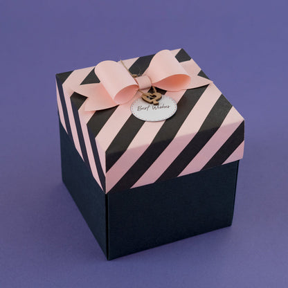 A two-layered baby pink and black striped Explosion Box with a pink ribbon on top, displaying a 'Best Wishes' tag.